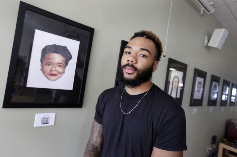 Jasaad Graves, wearing a black T-shirt, stands against a backdrop of portraits.