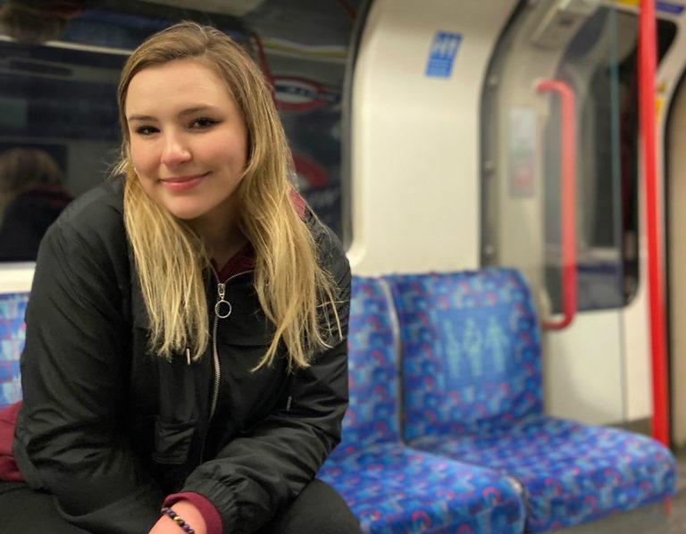 Caroline Garrow sits in a subway car wearing a black coat.