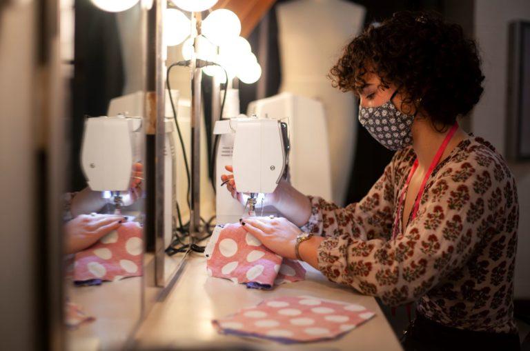 Maggie McGlenn, wearing a polka-dot mask, uses a sewing machine to work on pink polka-dot fabric..