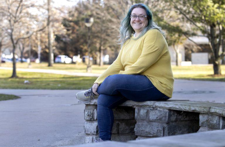 Deanna Donohoue sits on a stone bench and crosses her legs.