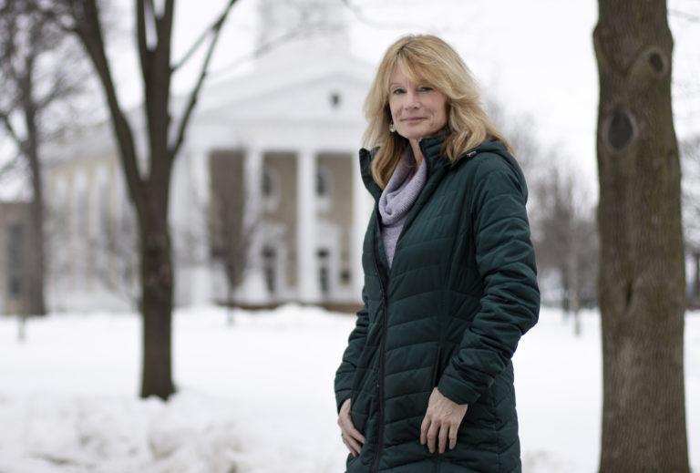 Patty Darling stands, wearing a black winter coat, against a backdrop of a snow-covered Main Hall Green.