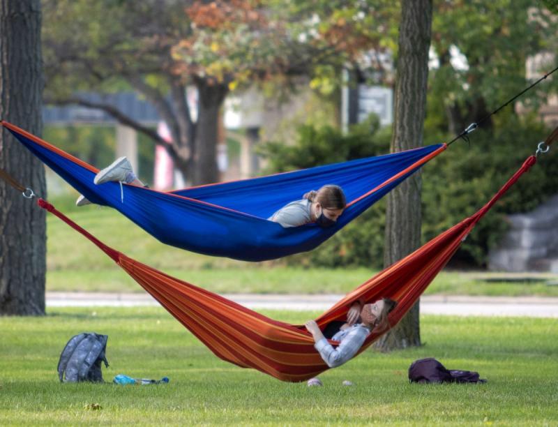 Two students talking while they hang in their own outdoor hammocks. 