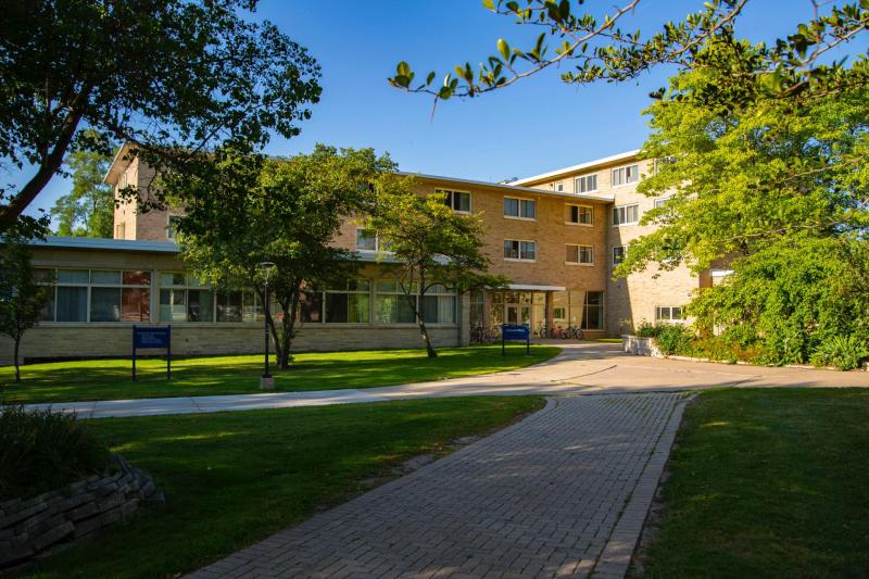 two brick roads leading to three-story brick building with green trees in foreground