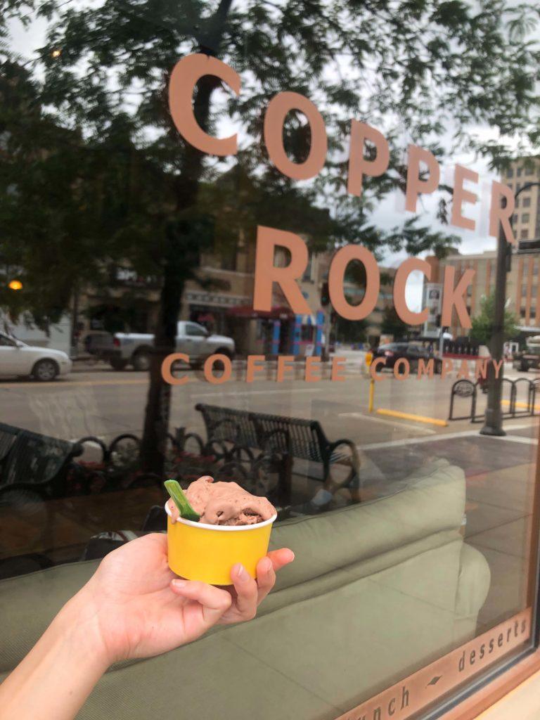 Hand holding an ice-cream cup in front of a Copper Rock Coffee sign 