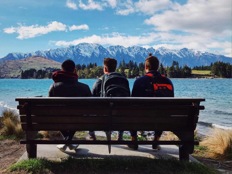 Students resting on bench by mountains and lake