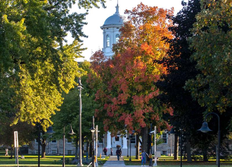 Scenic photo of campus with Main Hall's cupola peaks out from behind trees turning orange in fall.