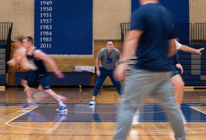 Lawrence's new men's basketball coach stands on sidelines while players jog across the court.