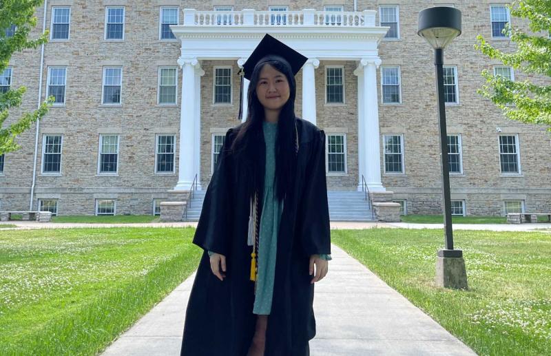 Doan Thu Thuy Nguyen in cap and gown in front of Main Hall.