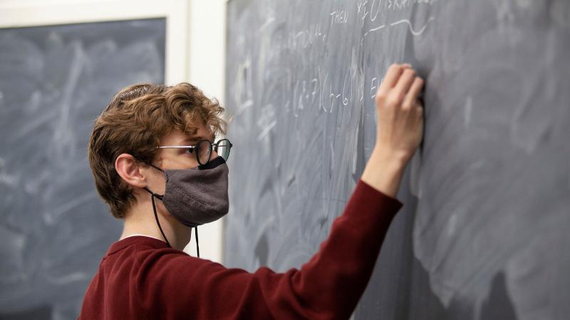 Student works on a math equation at the chalkboard