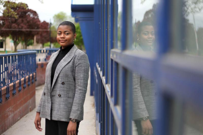 Shania Johnson. wearing a grey suit jacket, stands next to the blue windows of the Wriston Art Center.