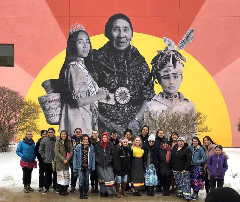 Native students stand in front of a colorful mural
