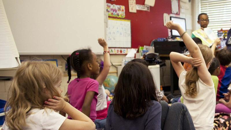 Children in a classroom listening and raising hands