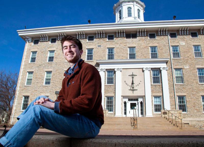 Eli Ferrell sits on a step with Main Hall in the background. 