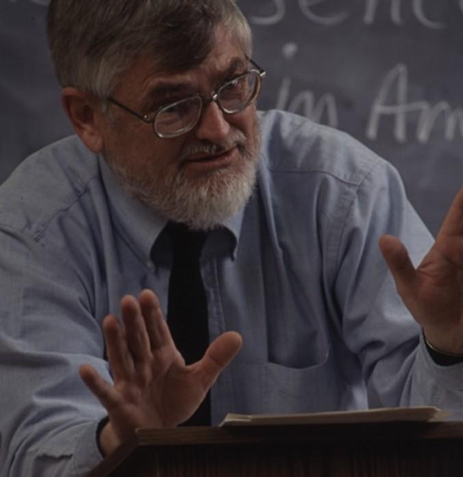 Peter Fritzell leans over a lectern while lecturing during class.