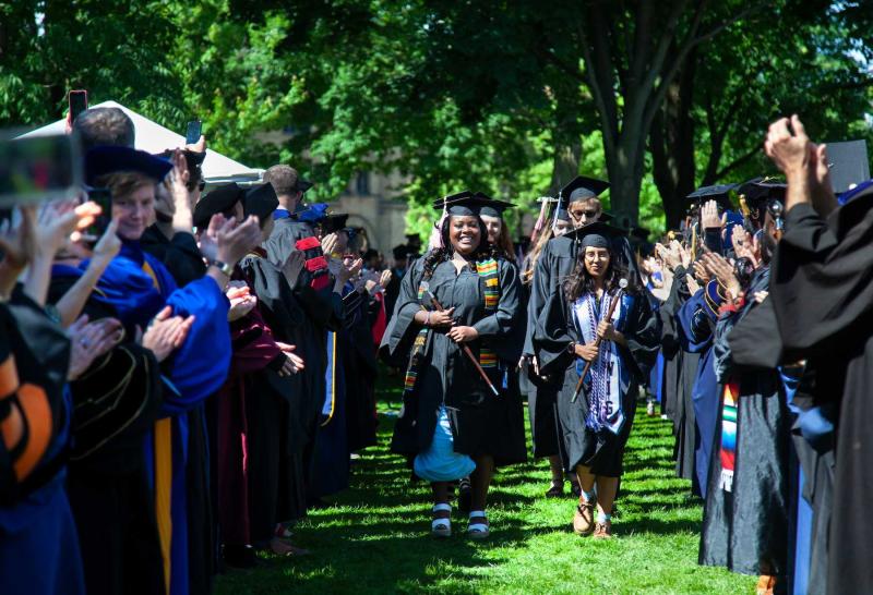 Graduates walk through the faculty line as faculty applaud during the processional at the start of Commencement.