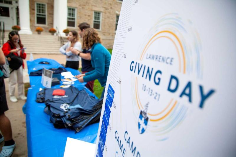 Students and staff give away t-shirts at a table on campus next to a Giving Day sign during 2021 Giving Day.
