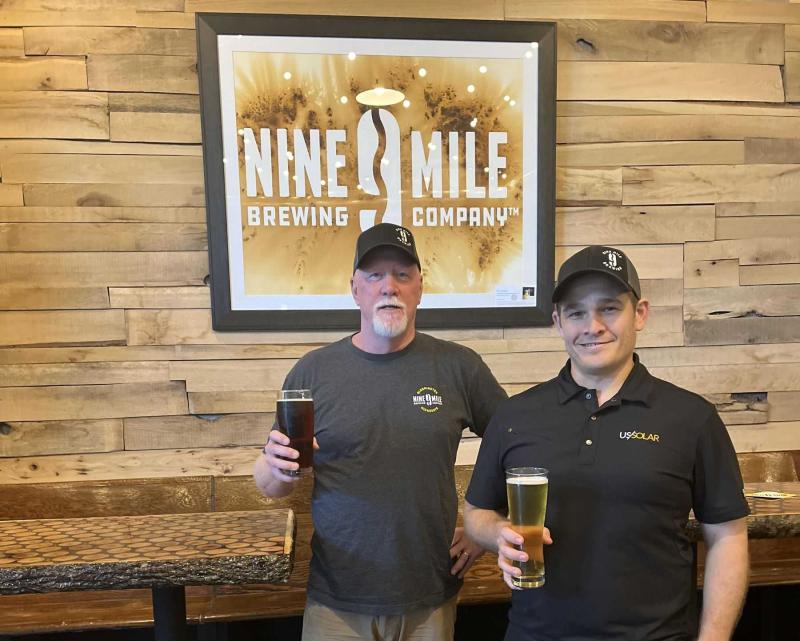 Bob Countryman and Ilan Klages-Mundt hold beers in front of a Nine Mile sign in their brewery.