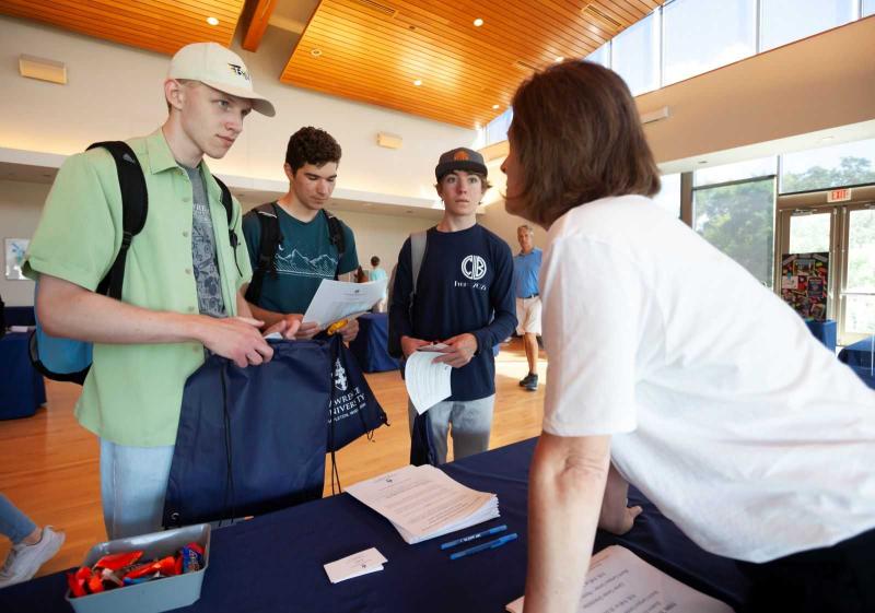 Henry Tibbetts-Zesbaugh, Ben Resnick, and Cormac Billick talk to a staff member at an information table during the Campus Resources Fair during New Student Move-in.