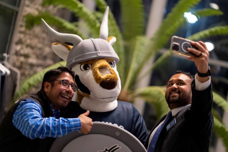 Two alumni take photos with the new antelope mascot at a Friday night Homecoming gathering.