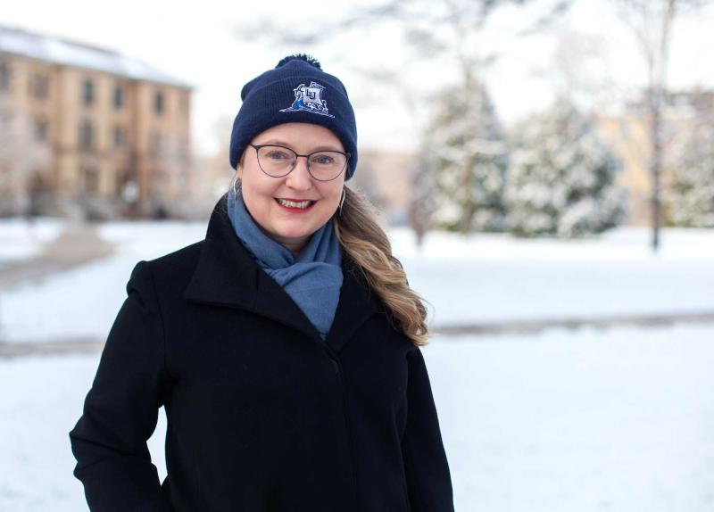 Nora Lewis wears a Lawrence winter cap and a black coat as she poses for a photo in the snow on Main Hall Green.