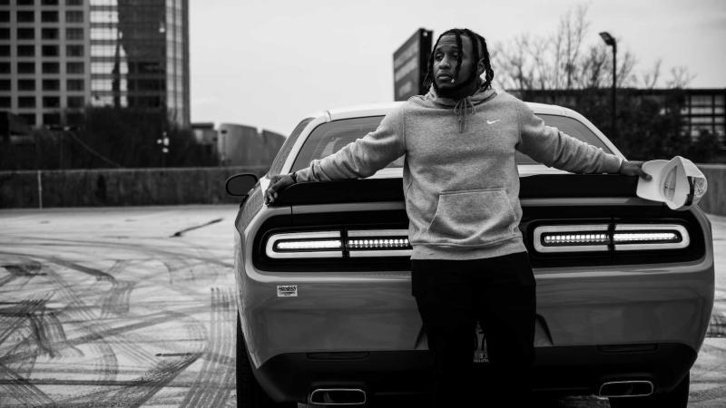 Wasonu Allen, a Lawrence alumnus who performs as Sonu., poses for a publicity photo behind a car.