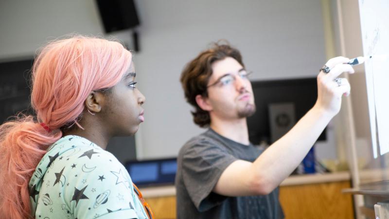A student instructing another student using a smartboard. 