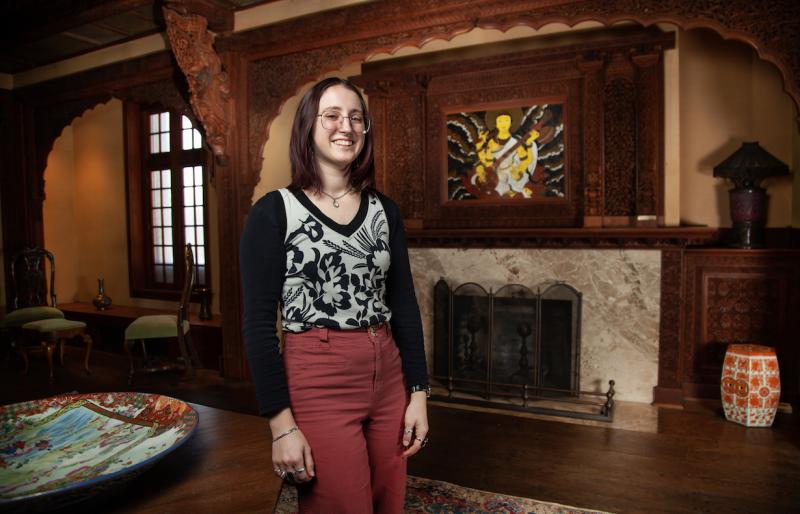 Melanie Shefchik stands in the Teakwood Room with the fireplace behind her.