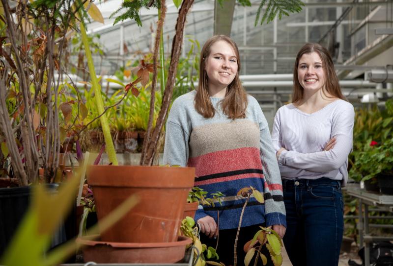 Amber Newman and Madeline Taylor stand in the greenhouse in Briggs Hall.