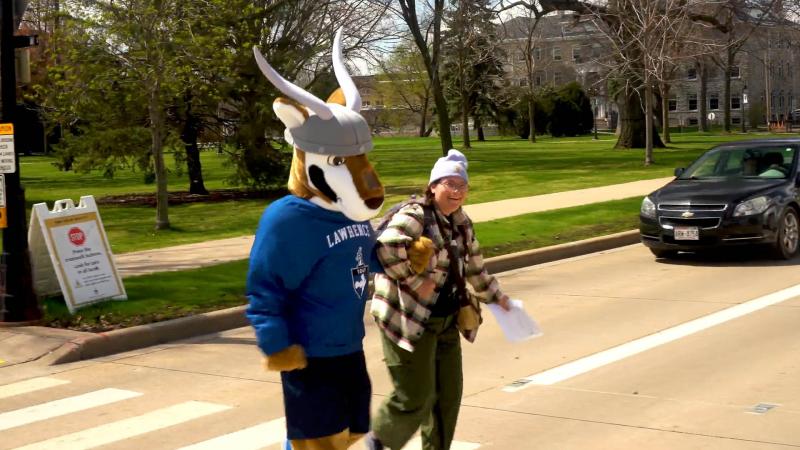 Lawrence mascot, Blu, helping a student across the crosswalk