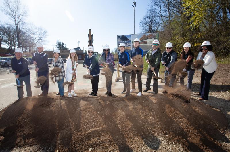 President Laurie Carter leads a group of 11 staff and students in throwing shovels of dirt at the groundbreaking ceremony.