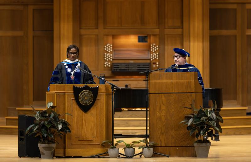 President Laurie A. Carter speaks at a podium on the stage of Memorial Chapel as Provost Peter Blitstein, at a second podium, looks on.