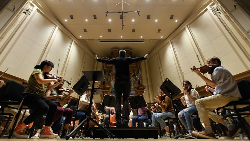 Conductor raises his arms to conduct orchestra on Lawrence Chapel stage