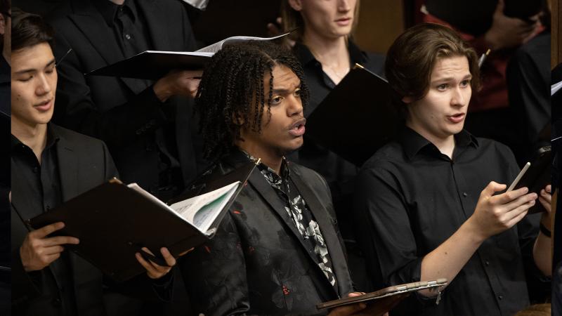 Choir members in concert black clothing holding black music folders sing on the Lawrence Chapel stage