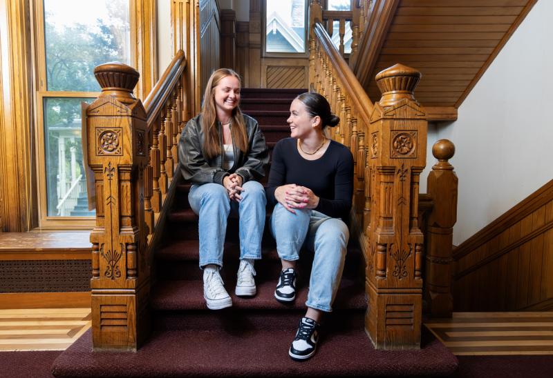 Emma Vasconez and Sydney Seeley talk on the stairs inside Lawrence's International House.