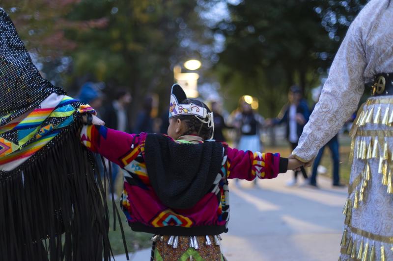 A child holds hands with other participants during the Indigenous Peoples' Day Celebration on Main Hall Green.
