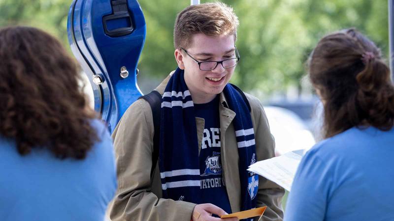 Smiling student wearing a Lawrence scarf and carrying a blue cello case gets his keys from Welcome Week staff