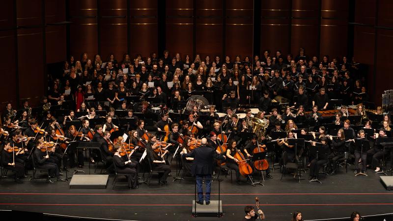 Combined instrumental and choral ensembles in performance, led by a conductor.