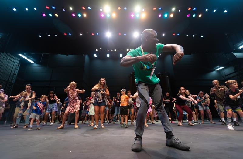 A man leading a group of families in a dance workshop.