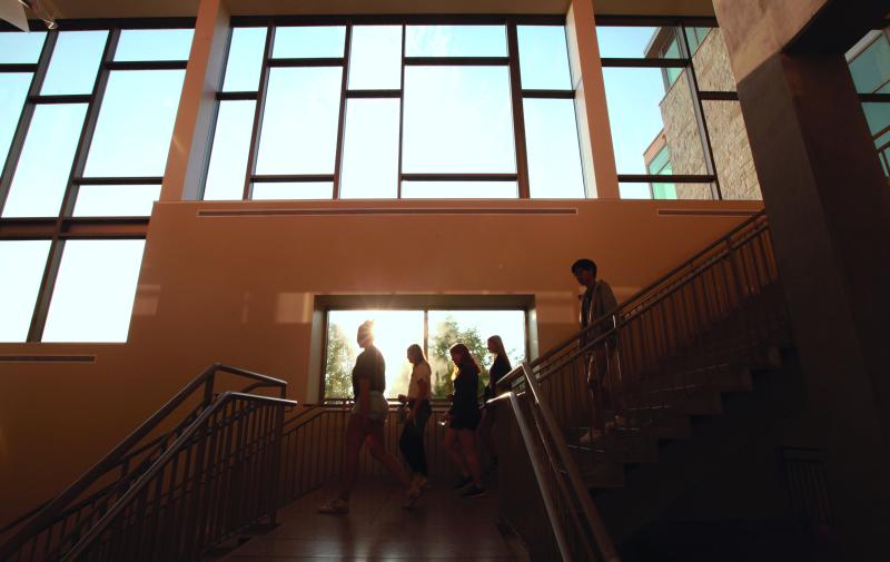 students walking down a large staircase in front of large windows with blue skies outside