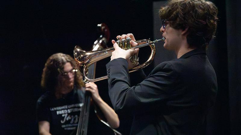 A musician playing flugelhorn, with a bassist in the background.