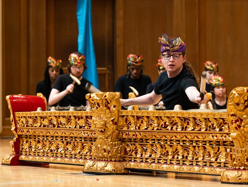 An ensemble of costumed musicians playing gold and red metallophone instruments.