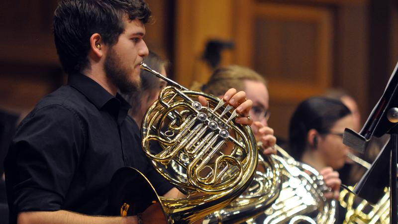 A row of musicians playing horn in concert.