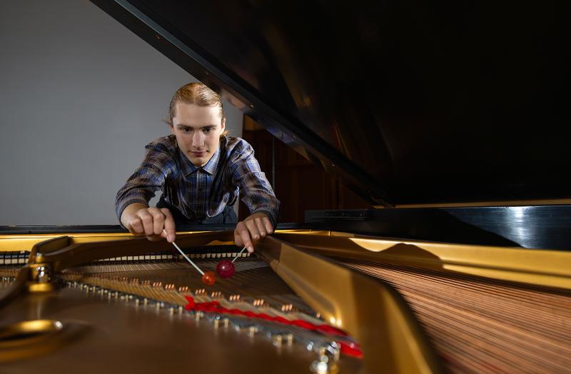A musician playing on the strings of a piano with a pair of percussion mallets.