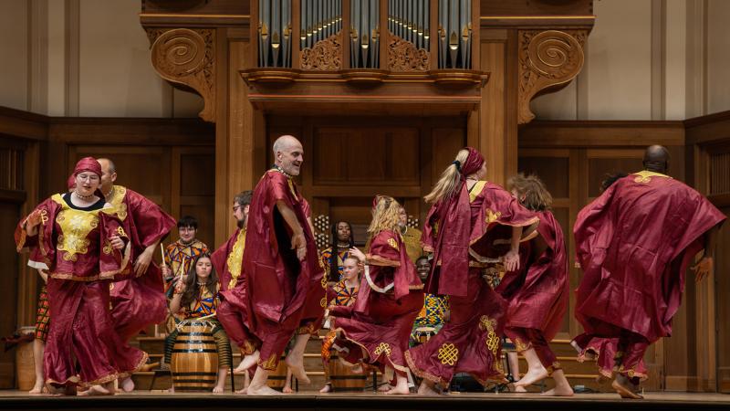 An ensemble of costumed dancers performing traditional West African dance on stage.