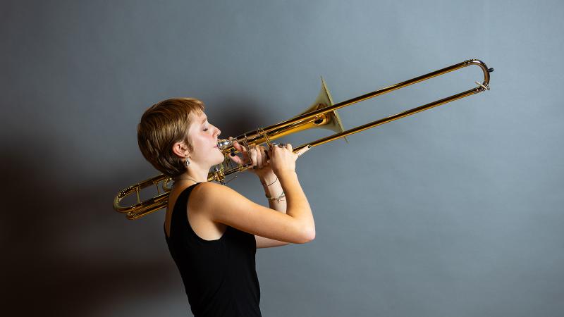 A student posing lengthwise with a trombone.