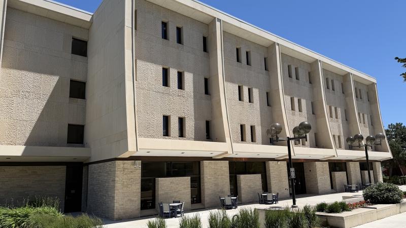 Image of the Mudd Library building from a front side angle. It's a sunny summer day and the plans in front are green.