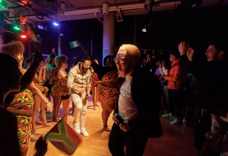 Students dancing at Cultural Expressions with some students wearing African clothing and a South African flag in the foreground