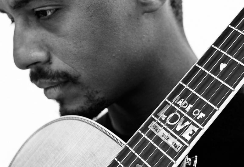 Ron Artis holds a guitar and looks to his right and down