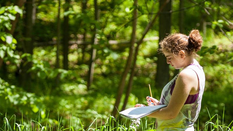 A student writes in a notebook during an outdoor lab session.
