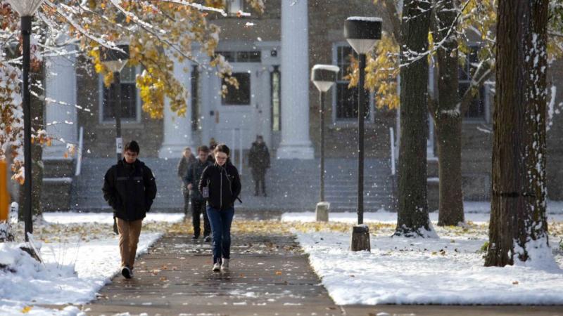 Students walk from Main Hall as snow falls on Main Hall Green.